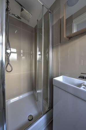 A modern bathroom with a glass-enclosed shower, a white sink, and a mirror above the sink. - CJ8 Medium Studio (London)