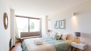 Een slaapkamer met een bed, nachtkastjes, een bankje en een raam.