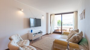 Een moderne woonkamer met een flatscreentelevisie, een bank, een fauteuil en een groot raam met gordijnen.