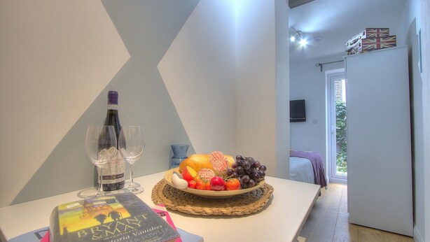 Ein Zimmer mit Esstisch, gedeckt mit einer Weinflasche, Gläsern, einem Buch und einer Obstplatte.