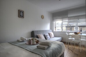 Un dormitorio con dos camas, una zona de comedor con mesa y sillas, y una ventana con vistas a edificios.