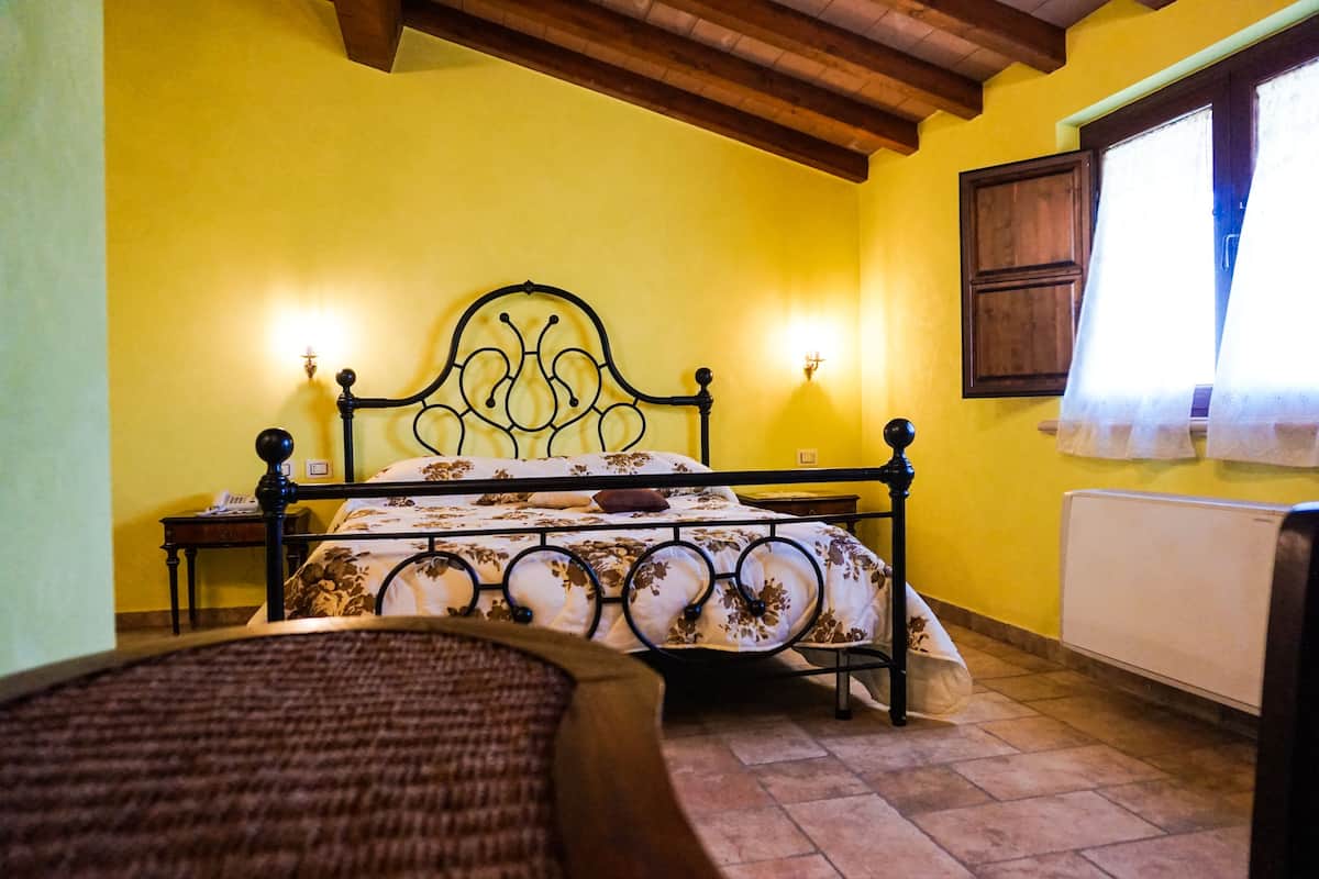 Une chambre à coucher avec un lit, des tables de chevet, un radiateur et une fenêtre avec des rideaux.
