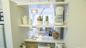A kitchen with white appliances, including a coffee maker, toaster, and kettle. There are shelves with decorative items and a window with plants. - Borges Apartment by Be Local Argentina (Buenos Aires)