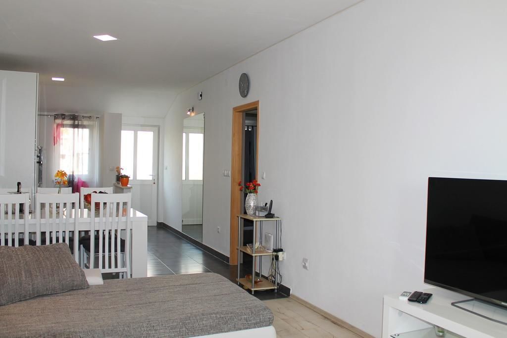 A modern living room with a large flat-screen TV, a white sofa, and a dining area with a white table and chairs.