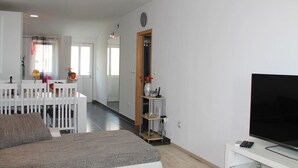 Ein modernes Wohnzimmer mit einem großen Flachbildfernseher, einem weißen Sofa und einem Essbereich mit weißem Tisch und Stühlen.