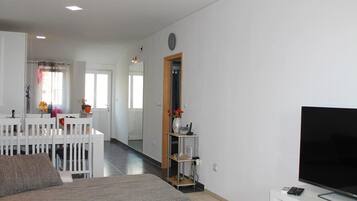 Una sala de estar moderna con un televisor de pantalla plana grande, un sofá blanco y una zona de comedor con una mesa y sillas blancas.