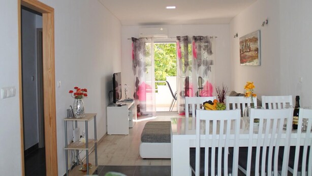 Ein modernes Wohnzimmer mit Essbereich, Fernseher und Blick ins Freie.