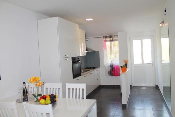 A modern kitchen with white cabinetry, a dining table with chairs, and a fruit bowl.