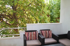 A balcony with wicker furniture and striped cushions, overlooking a lush green tree.