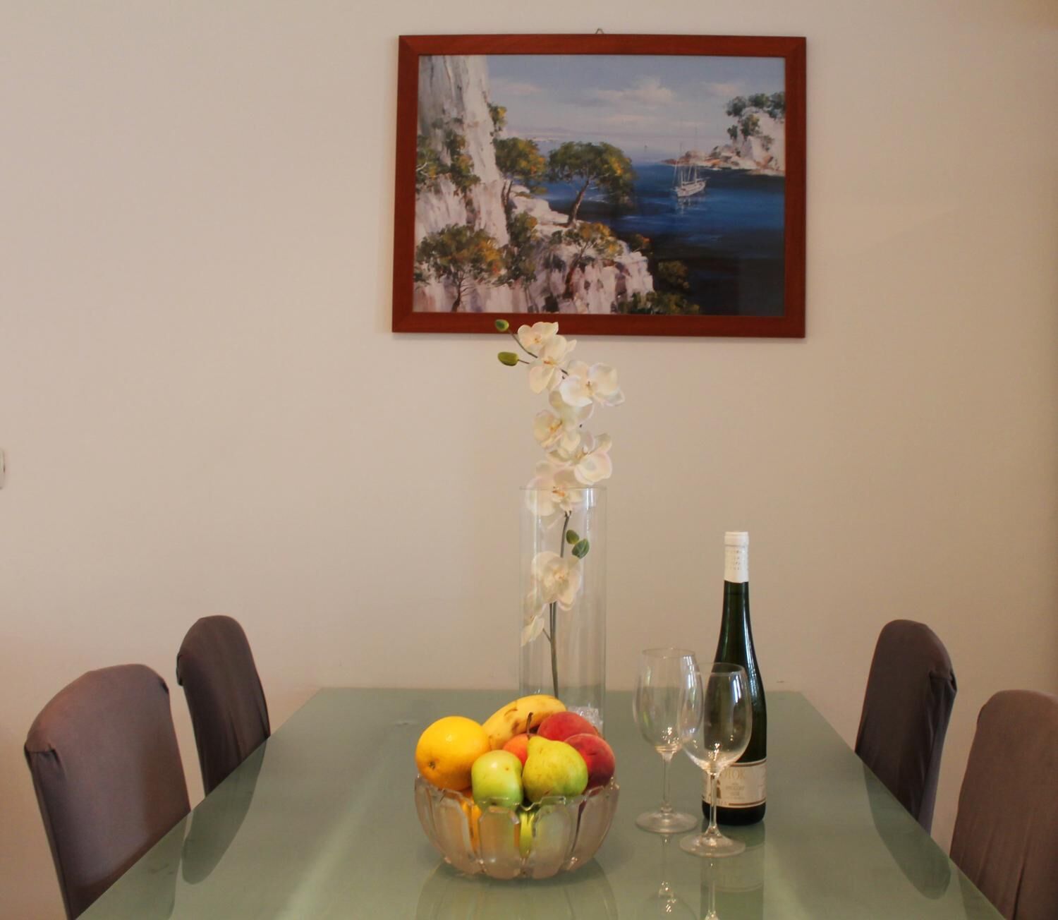 Una mesa de comedor con un frutero, una botella de vino y copas.