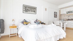 Hotellihuone, jossa on sänky, työpöytä, tuoli, pieni keittiö ja seinällä oleva taulu.