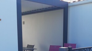 Un espace extérieur abrité, équipé d’une table et de chaises, d’une petite table et d’une chaise rouge.