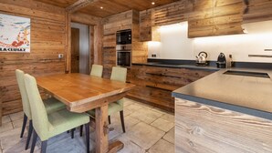 A wooden interior with a dining table, chairs, a kitchen with appliances, and a wooden ceiling. - Cozy 4* apartment, south terrace, near slopes, parking, Wi-Fi (La Clusaz)