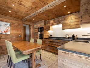 Un intérieur en bois comprenant une table à manger, des chaises, une cuisine équipée et un plafond en bois.