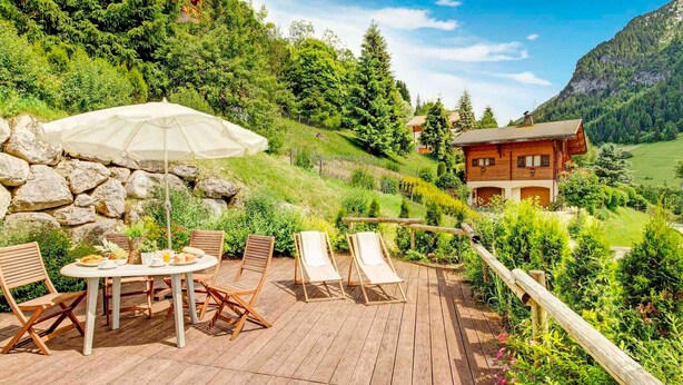 A wooden deck with a table and chairs, a white umbrella, and a wooden fence. - Cozy 4* apartment, south terrace, near slopes, parking, Wi-Fi (La Clusaz)