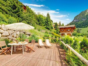 Un terrazzino in legno con tavolo e sedie, un ombrellone bianco e un recinto in legno.