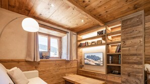 A cozy cabin interior with a wooden ceiling, a sofa, a coffee table, a bookshelf, and a window with a view of mountains. - Cozy 4* apartment, south terrace, near slopes, parking, Wi-Fi (La Clusaz)