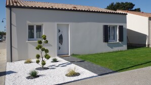 Une maison moderne de plain-pied, avec un toit en tuiles, une façade blanche et un petit jardin devant, composé de gravier et de plantes.