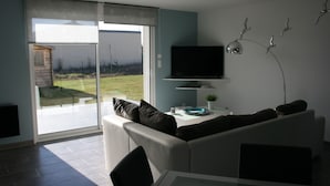Un salon moderne avec un canapé, un téléviseur à écran plat fixé au mur et une porte-fenêtre coulissante donnant sur une terrasse.