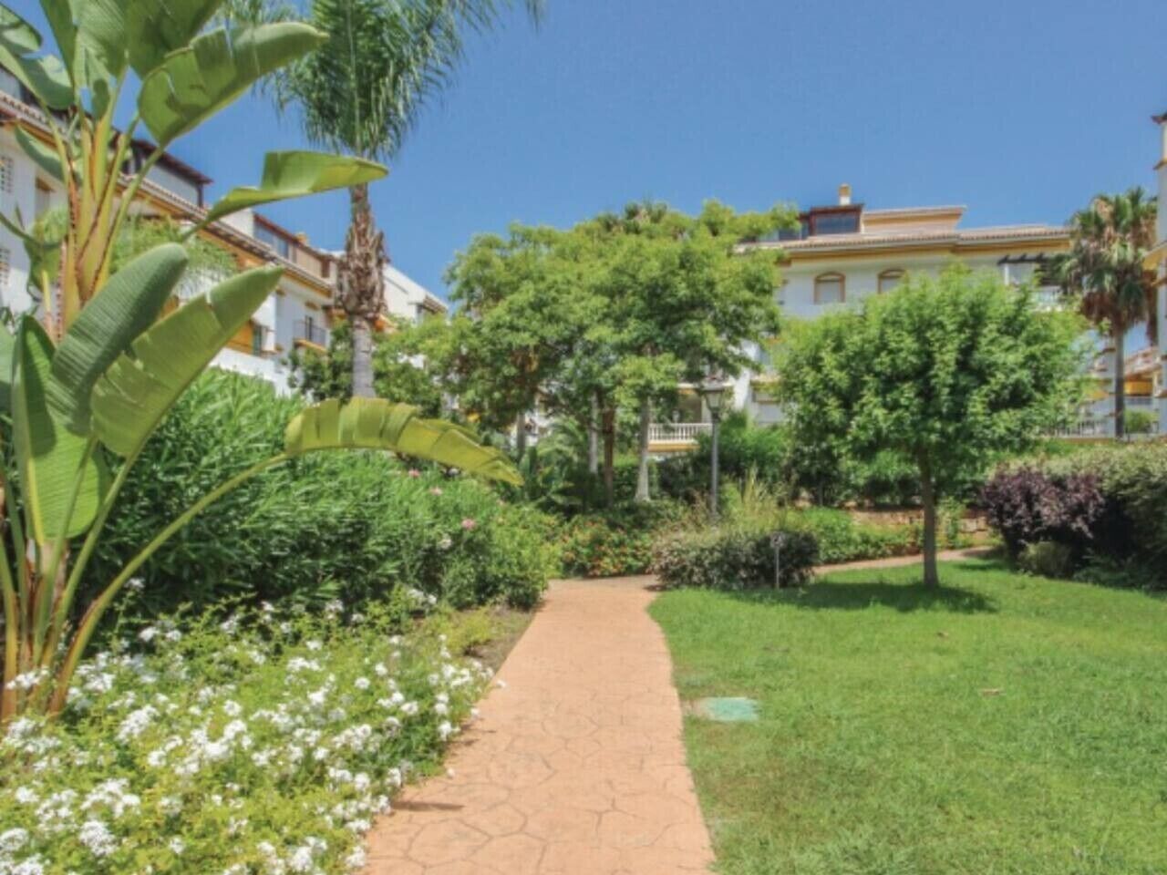 A pathway leading through a well-maintained garden with various plants and trees.