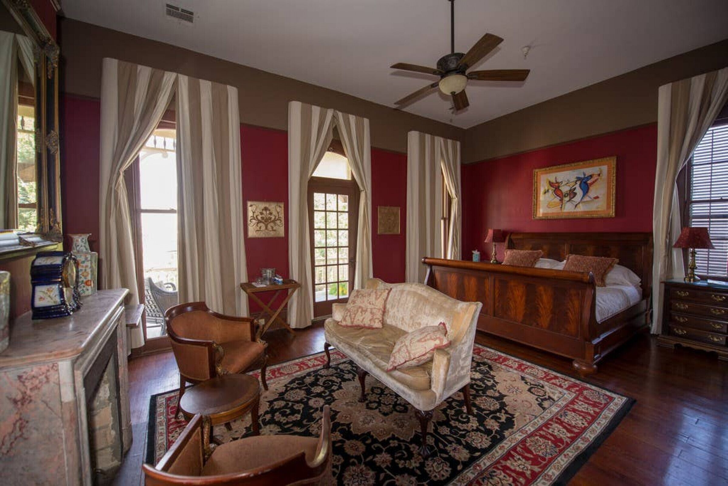 A room with a bed, a sofa, a chair, a fireplace, and a ceiling fan.