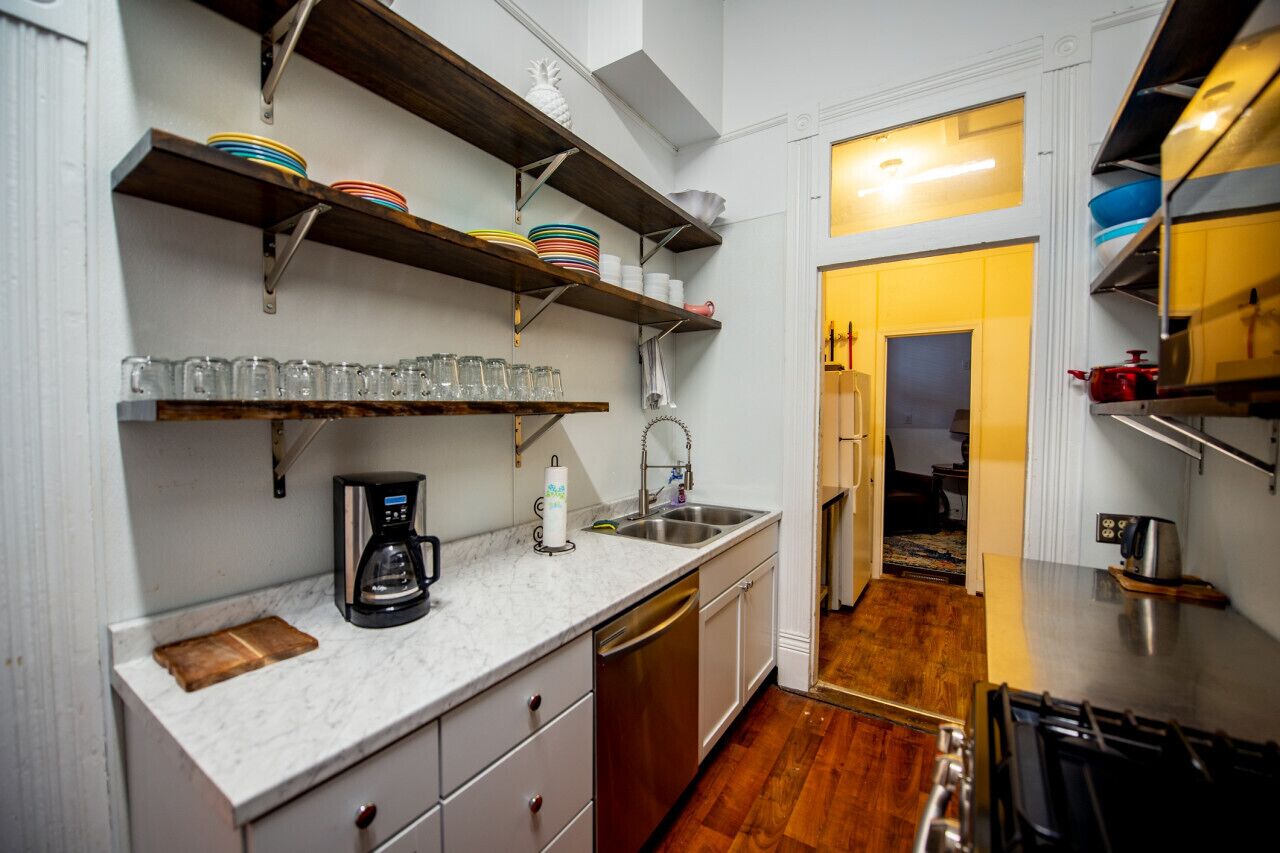 A compact kitchen with a coffee maker, shelves with dishes, and a sink.