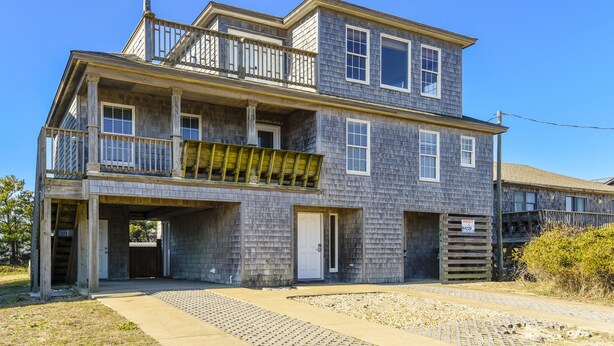 A two-story building with a balcony on the upper floor, a garage entrance, and a driveway leading to the front door. - Semi Ocean Front in Nags Head NC with Private Pool! (Nags Head)