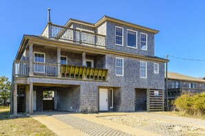 A two-story building with a balcony on the upper floor, a garage entrance, and a driveway leading to the front door. - Semi Ocean Front in Nags Head NC with Private Pool! (Nags Head)
