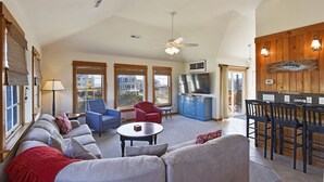 A spacious living room with a sofa set, a red armchair, a blue armchair, a dining table with chairs, and a kitchen area with a stove and cabinets. - Semi Ocean Front in Nags Head NC with Private Pool! (Nags Head)