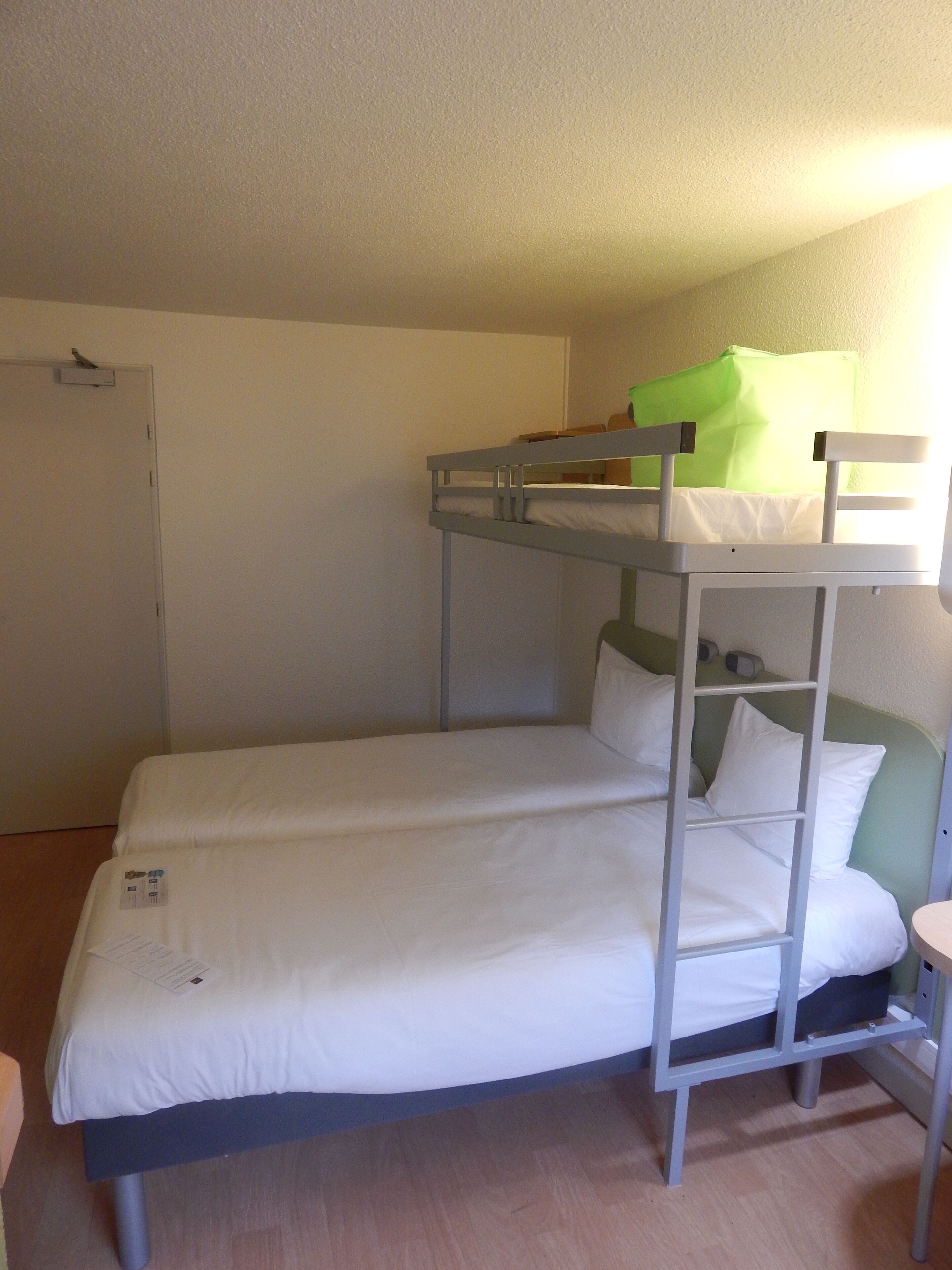 A bunk bed room with a door, a small stool, and a green object on the top bunk.