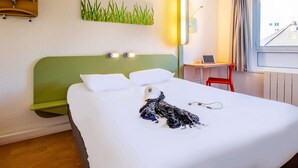 A hotel room with a bed, a desk, a chair, a lamp, and a window with a view. - ibis budget Limoges (Limoges)