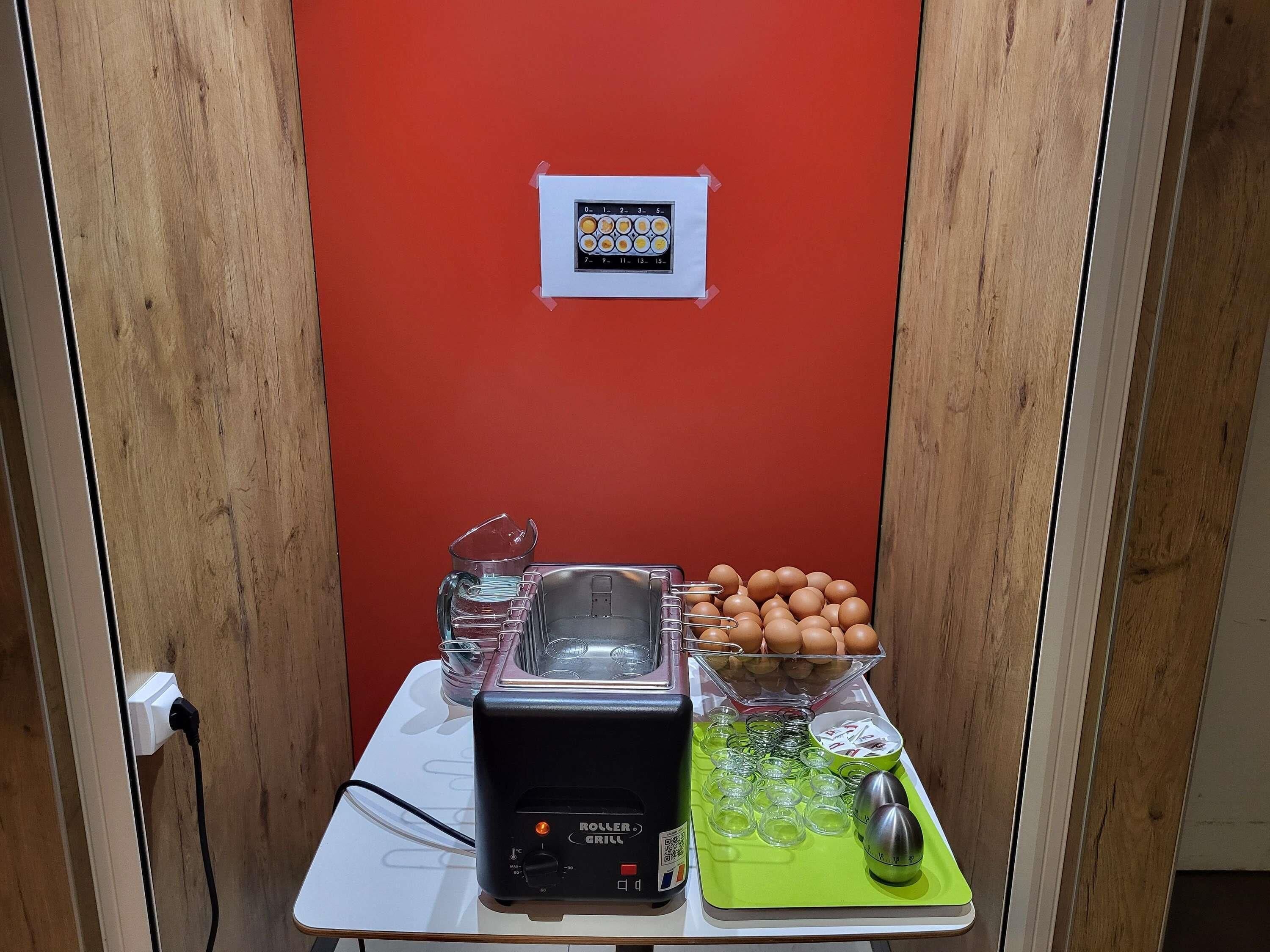 Una kitchenette con un tostador, un cuenco de huevos, una jarras de vidrio y una tabla de cortar verde.