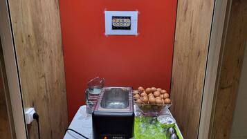 Una kitchenette con un tostador, un cuenco de huevos, una jarras de vidrio y una tabla de cortar verde.