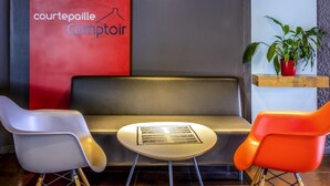 A modern interior with a red wall, a grey bench, and two chairs. A small table is in front of the bench. - ibis budget Limoges (Limoges)