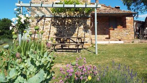 A stone building with a wooden pergola in a garden. - Charming farmhouse apartment with garden, pool and views (Casole d'Elsa)