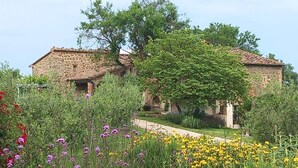 A stone building with a tiled roof, surrounded by a garden with various flowers and trees. - Charming farmhouse apartment with garden, pool and views (Casole d'Elsa)