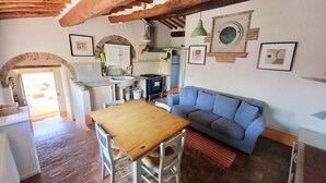 A rustic kitchen with a wooden table and chairs, a blue sofa, and a stone fireplace. - Charming farmhouse apartment with garden, pool and views (Casole d'Elsa)