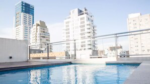 Ein Pool auf dem Dach mit Glasgeländer, umgeben von Hochhäusern.