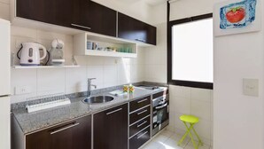 Eine moderne Küche mit dunklen Schränken, einer Granit Arbeitsplatte, einer Edelstahl-Spüle, einem Wasserkocher und einem kleinen gelben Hocker.