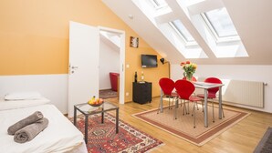 Un dormitorio moderno con tragaluces, una zona de comedor con sillas rojas, un televisor y una pequeña mesa con fruta.