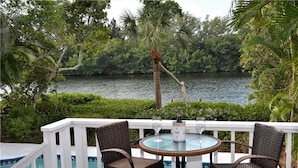 A balcony with a pool, two wicker chairs, and a table with a bottle and glass. - 4BR Siesta Key lagoon home w/ heated pool (Sarasota)