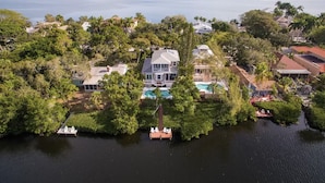 A large house with a swimming pool surrounded by dense greenery and a body of water. - 4BR Siesta Key lagoon home w/ heated pool (Sarasota)