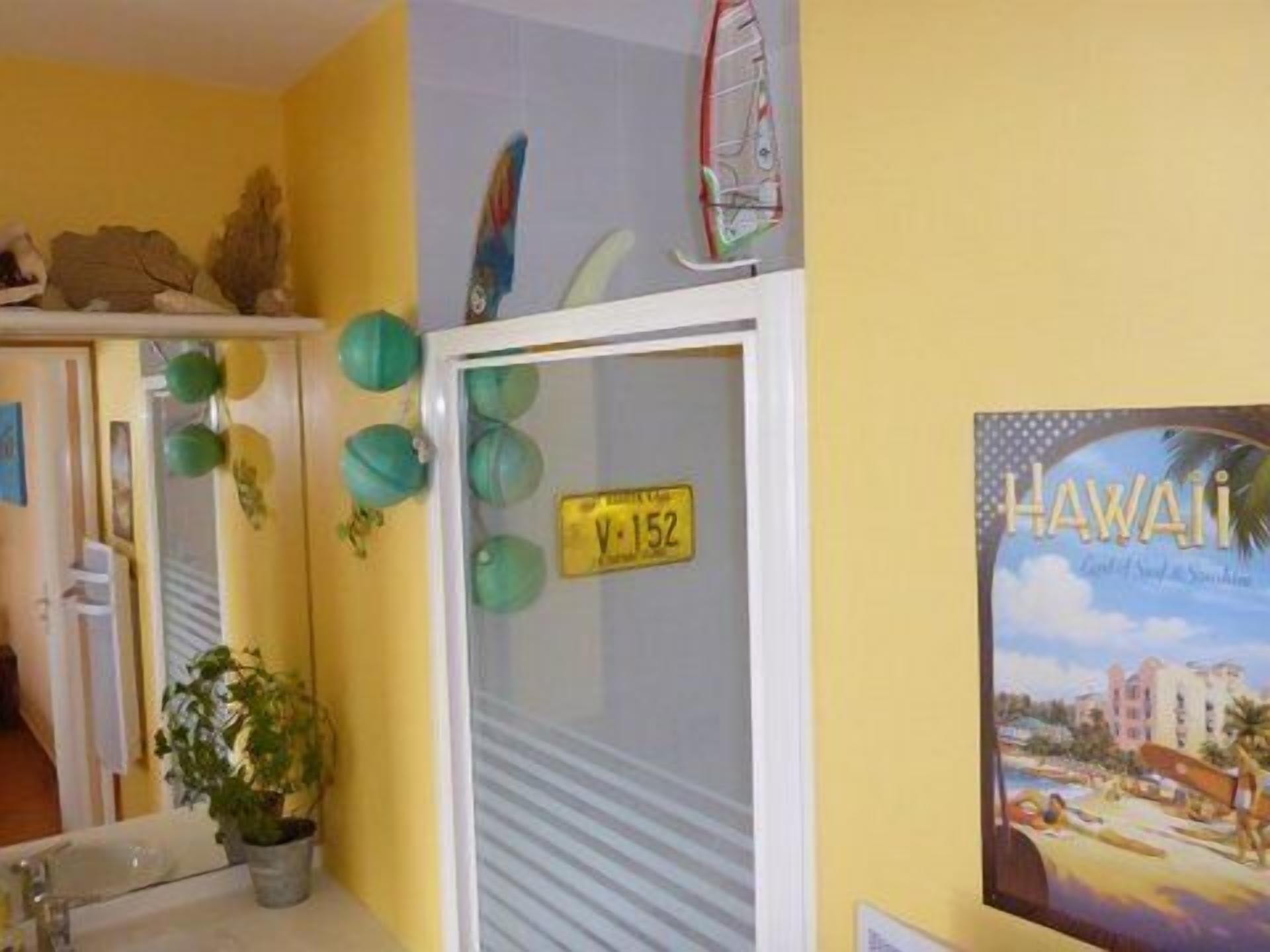 A bathroom with a yellow wall, a white sink, a mirror, and a framed picture of Hawaii.