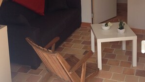 A small, cozy room with a black sofa, a red throw pillow, a white coffee table with two small plants, and a wooden chair. - Cottage 100 meters from the beach (Le Minihic-Sur-Rance)
