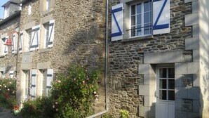 A stone building with multiple windows, some with shutters, and a small garden area with pink flowers. - Cottage 100 meters from the beach (Le Minihic-Sur-Rance)