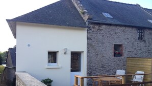 A two-story house with a wooden deck, a stone wall, and a small garden. - Cottage 100 meters from the beach (Le Minihic-Sur-Rance)