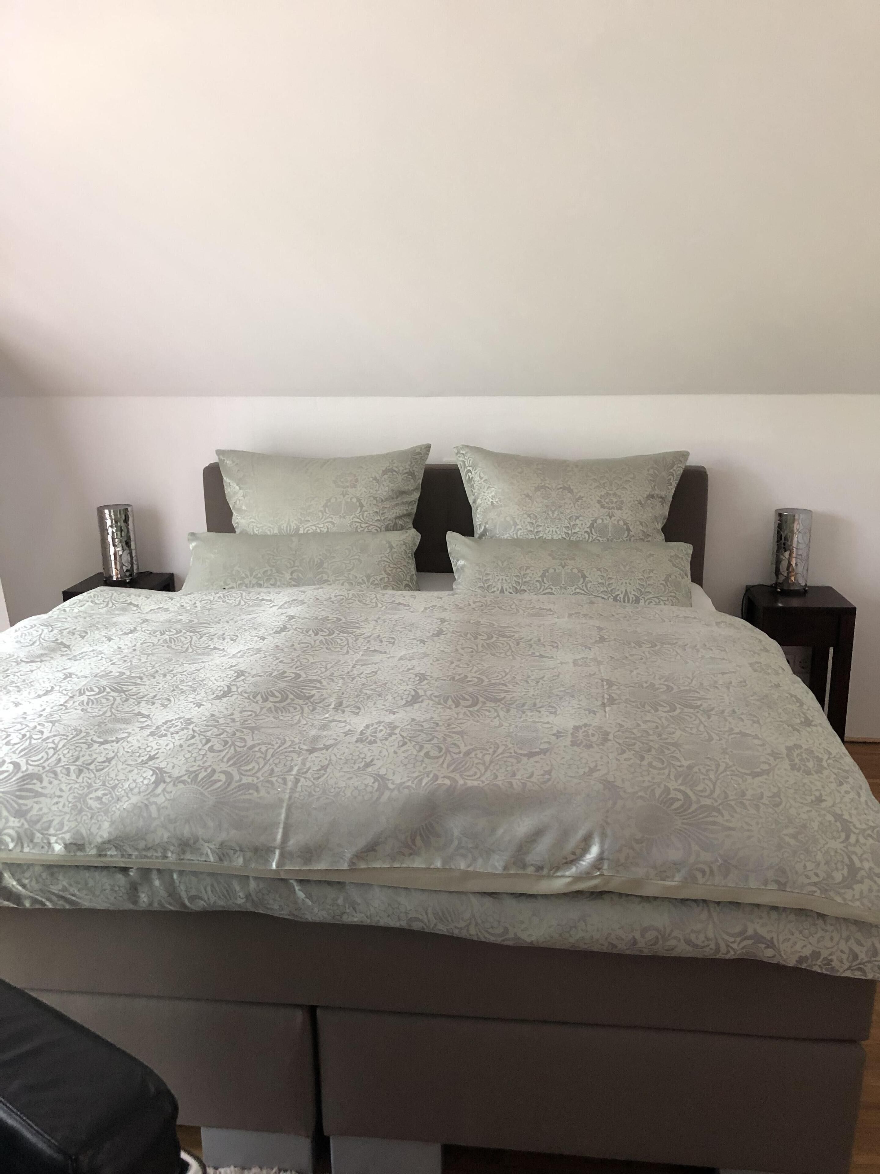 Un lit bien fait, recouvert d’une couvre-lit à motifs et agrémenté d’oreillers, avec deux tables de chevet de chaque côté, sur lesquelles sont posées des lampes.