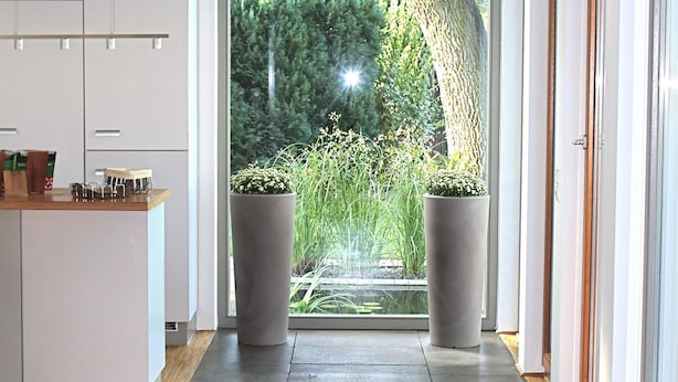 Une cuisine moderne avec des meubles blancs, un plan de travail en bois et une grande fenêtre donnant sur un jardin.