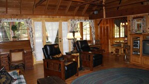 L’intérieur d’un chalet rustique, avec des murs en bois, un plafond haut et un coin salon confortable agrémenté de fauteuils en cuir et d’un canapé.