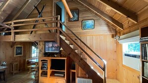L’intérieur d’un chalet en bois, avec un escalier, des murs en bois, un téléviseur et une bibliothèque.